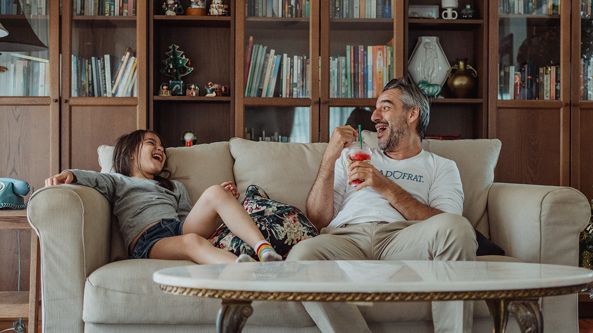 Father and daughter laughing while sitting their couch in the living room.