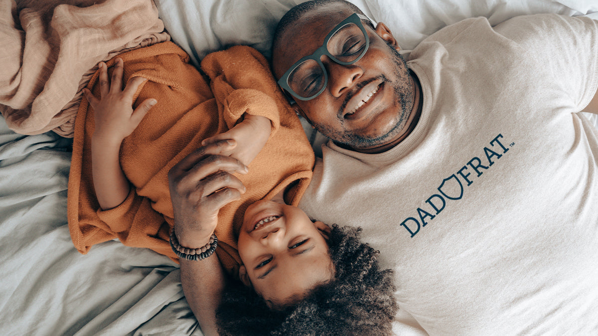 Dad and son laughing while laying on their backs in bed.