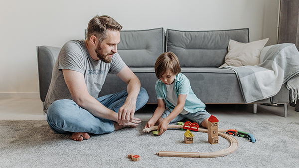 Father and son playing with a toy train in their living room.